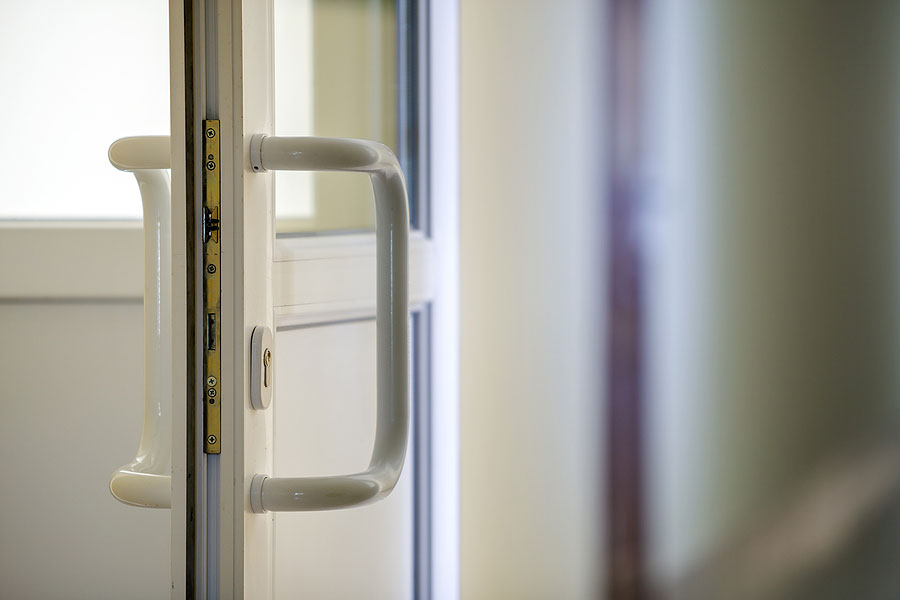 White plastic door detail with metal lock, handle and transparent glass on blurred interior background.