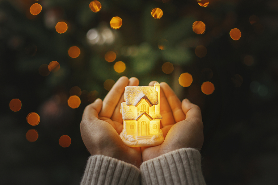 Little glowing house in hands on background of illuminated christmas tree lights