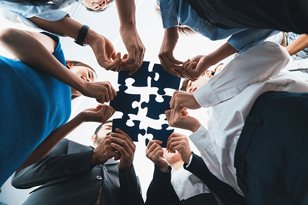 Below view of diverse corporate officer workers collaborate in office connecting puzzle pieces as partnership and teamwork concept. Unity and synergy in business idea by merging jigsaw puzzle. Concord